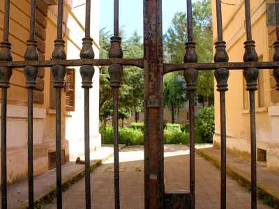 Sul lato opposto invece, quasi a voler dare una boccata d'aria alla rigida monotonia del poligono, interviene una cancellata in ferro, in gran parte sporca di ruggine, oltre la quale si intravede un fitto giardino che avvolge completamente i cortili interni dell'abitato